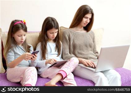 Family (mother and two daughters) watching phone and laptop (gadgets)