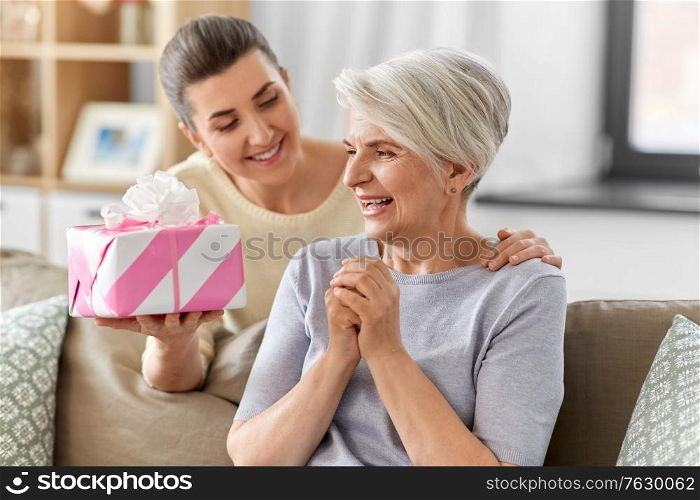 family, mother&rsquo;s day and birthday concept - happy smiling adult daughter giving present to her senior mother at home. adult daughter giving present to her senior mother