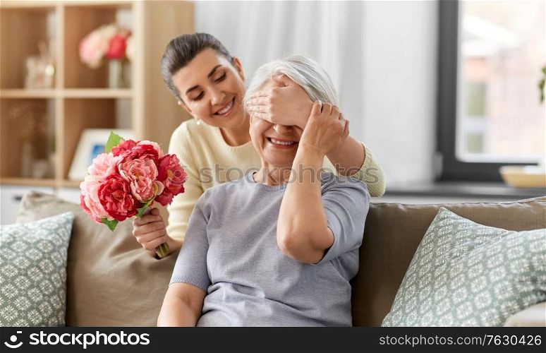 family, mother&rsquo;s day and birthday concept - happy smiling adult daughter giving flowers to her senior mother at home. adult daughter giving flowers to old mother