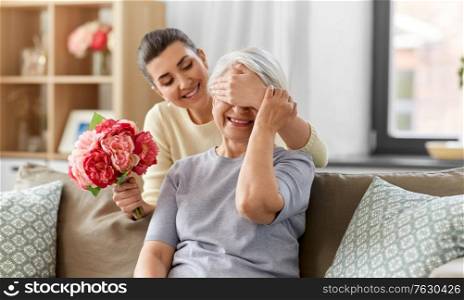 family, mother&rsquo;s day and birthday concept - happy smiling adult daughter giving flowers to her senior mother at home. adult daughter giving flowers to old mother