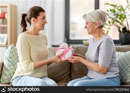 family, mother&rsquo;s day and birthday concept - happy smiling adult daughter giving present to her senior mother at home. adult daughter giving present to her senior mother