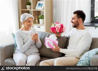 family, mother&rsquo;s day and birthday concept - smiling adult son giving present and flowers to his senior mother at home. son giving present and flowers to senior mother