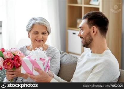 family, mother&rsquo;s day and birthday concept - smiling adult son giving present and flowers to his senior mother at home. son giving present and flowers to senior mother