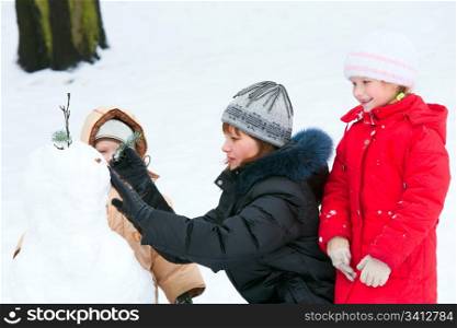 Family (mother with small children) sculpting snowmen in winter city park