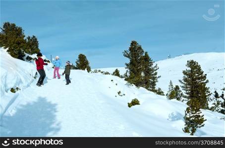 Family (mother with two children) plays at snowballs on winter mountain slope