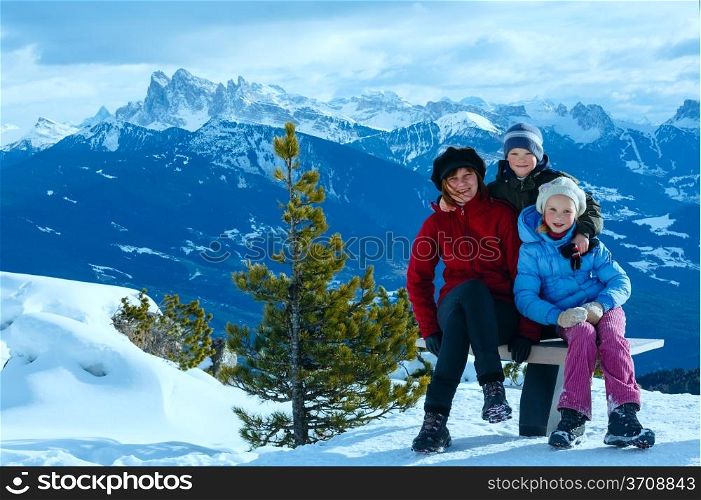Family (mother with two children) take a walk on winter mountain slope (view from Rittner Horn on Puez Geislergruppe on left, Italy)