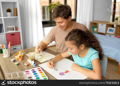 family, motherhood and leisure concept - happy smiling father spending time with his little daughter and drawing with colors at home. happy father with little daughter drawing at home