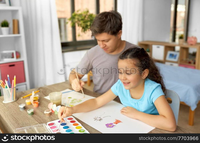 family, motherhood and leisure concept - happy smiling father spending time with his little daughter and drawing with colors at home. happy father with little daughter drawing at home