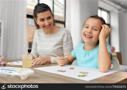 family, motherhood and leisure concept - happy smiling mother spending time with her little daughter drawing or painting wooden chipboard items with colors at home. happy mother with little daughter drawing at home