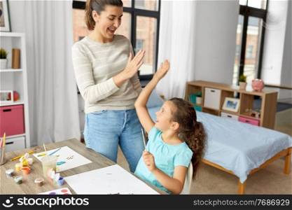 family, motherhood and leisure concept - mother spending time with her little daughter drawing with colors and making high five gesture at home. mother with daughter drawing and making high five