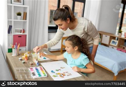 family, motherhood and leisure concept - mother spending time with her little daughter drawing or painting wooden chipboard items with colors at home. mother with little daughter drawing at home