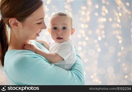 family, motherhood and parenthood concept - close up of happy smiling young mother with little baby over lights background. happy young mother with little baby over lights