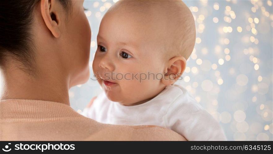 family, motherhood and people concept - close up of happy little baby boy with mother over holidays lights background. close up of happy baby with mother over lights