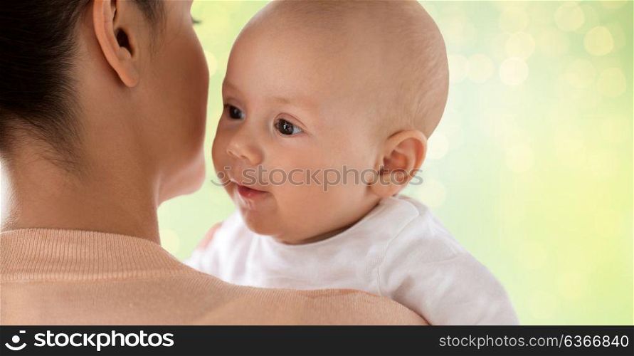 family, motherhood and people concept - close up of happy little baby boy with mother over green lights background. close up of happy baby with mother over green