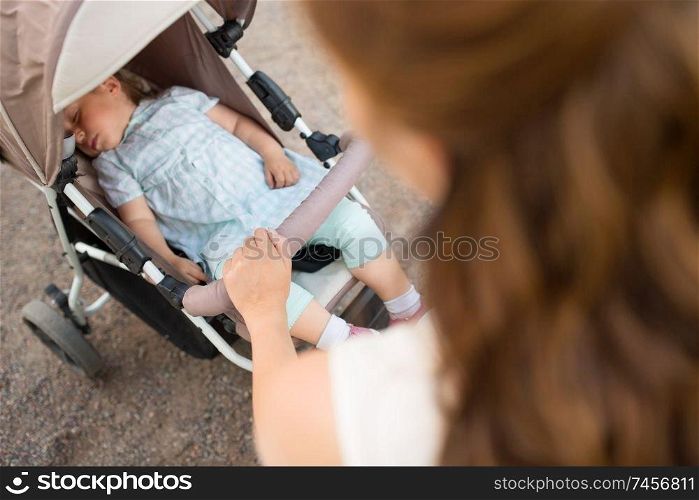 family, motherhood and people concept - close up of mother with child sleeping in stroller walking at summer park. mother with child in stroller walking at park