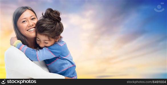 family, motherhood and people concept - happy mother and daughter hugging over evening sky background. happy mother and daughter hugging over evening sky. happy mother and daughter hugging over evening sky