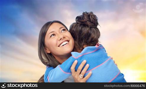 family, motherhood and people concept - happy mother and daughter hugging over evening sky background. happy mother and daughter hugging over evening sky. happy mother and daughter hugging over evening sky