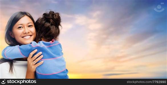 family, motherhood and people concept - happy mother and daughter hugging over evening sky background. happy mother and daughter hugging over evening sky