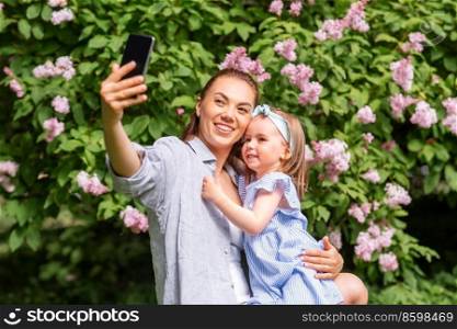 family, motherhood and people concept - happy mother and little daughter with smartphone taking selfie at summer park or garden. happy mother with daughter taking selfie at park