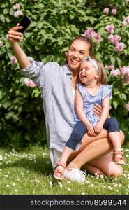 family, motherhood and people concept - happy mother and little daughter with smartphone taking selfie at summer park or garden. happy mother with daughter taking selfie at park