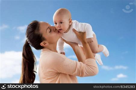 family, motherhood and people concept - happy mother kissing little baby boy over blue sky and clouds background. happy mother kissing little baby boy over sky