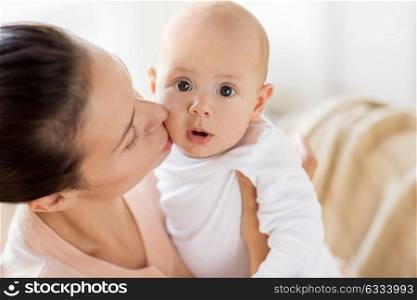family, motherhood and people concept - happy mother kissing little baby boy at home. happy mother kissing little baby boy at home