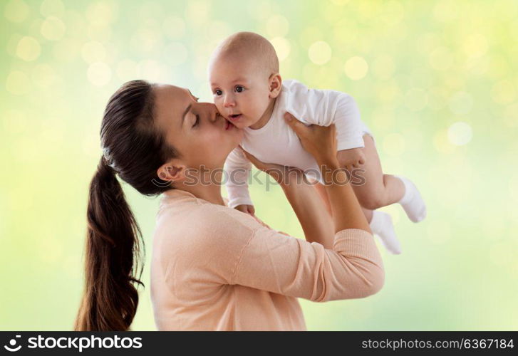 family, motherhood and people concept - happy mother kissing little baby boy over green lights background. happy mother kissing little baby boy over green