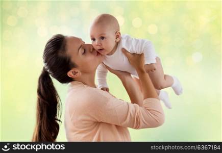 family, motherhood and people concept - happy mother kissing little baby boy over green lights background. happy mother kissing little baby boy over green