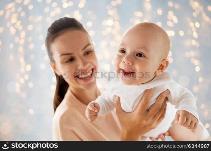 family, motherhood and people concept - happy mother playing with little baby boy over holidays lights background. happy mother playing with little baby over lights