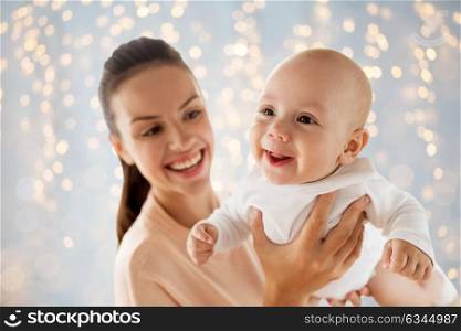 family, motherhood and people concept - happy mother playing with little baby boy over holidays lights background. happy mother playing with little baby over lights