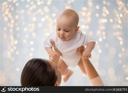 family, motherhood and people concept - happy mother playing with little baby boy over holidays lights background. happy mother playing with little baby boy over lights