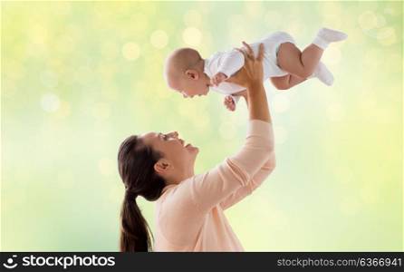 family, motherhood and people concept - happy mother playing with little baby boy over green lights background. happy mother playing with little baby over green