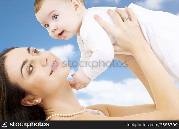 family, motherhood and people concept - happy mother playing with little baby over sky background. happy mother playing with little baby boy