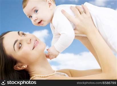 family, motherhood and people concept - happy mother playing with little baby over sky background. happy mother playing with little baby boy