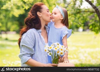 family, motherhood and people concept - happy mother with chamomile flowers kissing little daughter at summer park or garden. happy mother and daughter with chamomiles at park