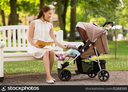 family, motherhood and people concept - happy mother with child in stroller reading book at summer park. mother with child in stroller reading book at park