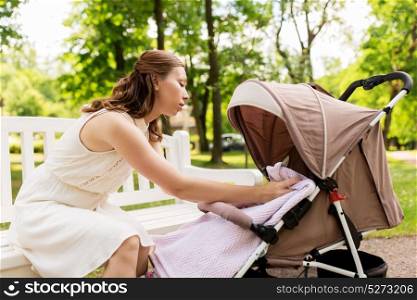 family, motherhood and people concept - happy mother with child in stroller at summer park. happy mother with child in stroller at summer park