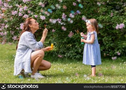family, motherhood and people concept - happy mother with little daughter blowing soap bubbles at summer park or garden. mother with daughter blowing soap bubbles at park