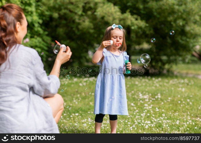 family, motherhood and people concept - happy mother with little daughter blowing soap bubbles at summer park or garden. mother with daughter blowing soap bubbles at park