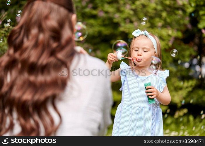 family, motherhood and people concept - happy mother with little daughter blowing soap bubbles at summer park or garden. mother with daughter blowing soap bubbles at park