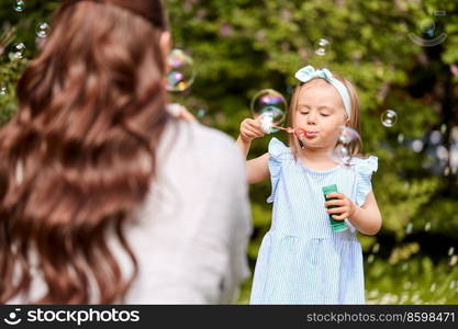 family, motherhood and people concept - happy mother with little daughter blowing soap bubbles at summer park or garden. mother with daughter blowing soap bubbles at park