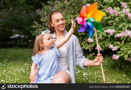 family, motherhood and people concept - happy mother with little daughter playing with pin wheel toy at summer park or garden. happy mother and daughter with pin wheel at park