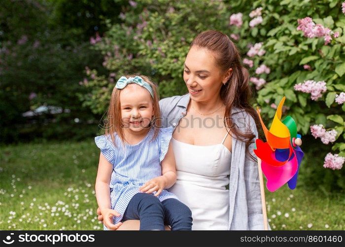 family, motherhood and people concept - happy mother with little daughter playing with pin wheel toy at summer park or garden. happy mother and daughter with pin wheel at park
