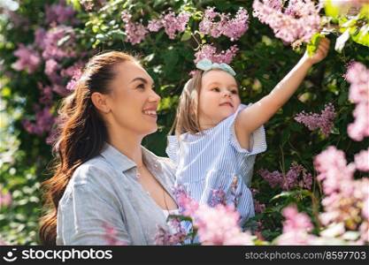 family, motherhood and people concept - happy mother with little daughter touching lilac flowers at summer park or garden. happy mother with little daughter at summer park