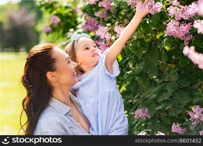 family, motherhood and people concept - happy mother with little daughter touching lilac flowers at summer park or garden. happy mother with little daughter at summer park