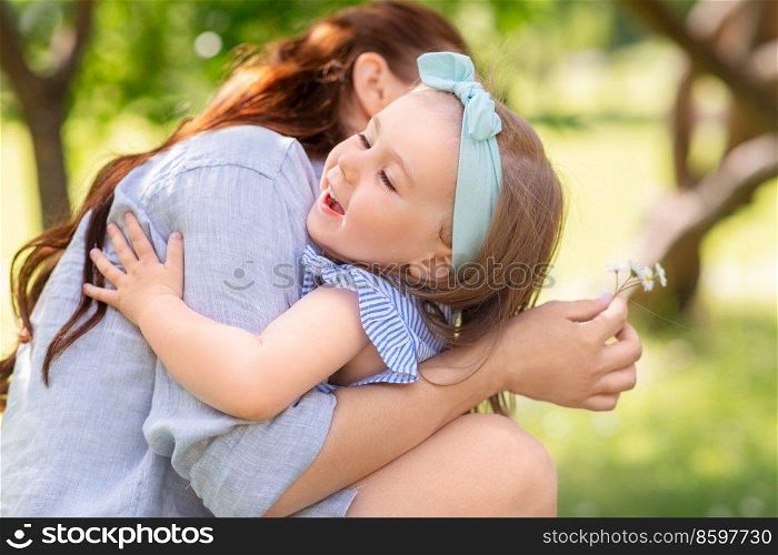 family, motherhood and people concept - happy mother with little daughter with daisy flowers hugging at summer park or garden. happy mother and daughter with flowers at park