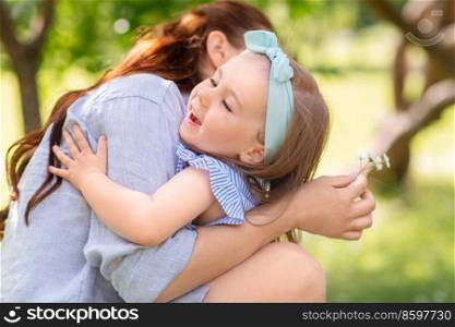 family, motherhood and people concept - happy mother with little daughter with daisy flowers hugging at summer park or garden. happy mother and daughter with flowers at park