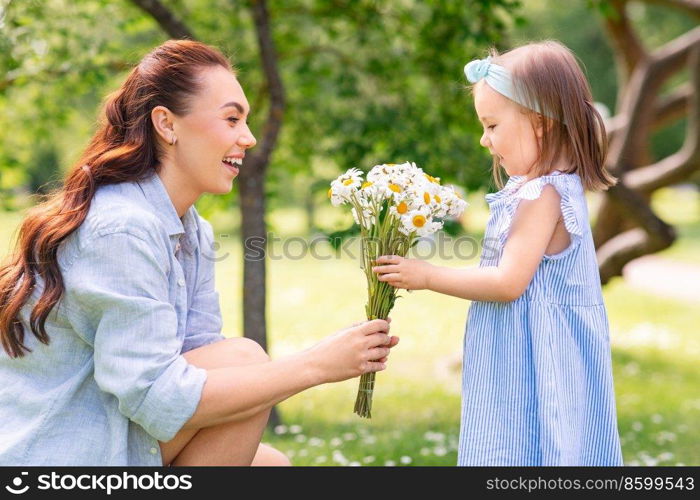 family, motherhood and people concept - happy mother with little daughter with chamomile flowers at summer park or garden. happy mother and daughter with chamomiles at park