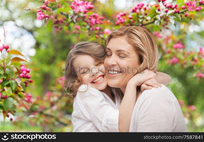family, motherhood and people concept - happy smiling mother and daughter hugging over cherry blossom background. happy mother and daughter hugging over garden