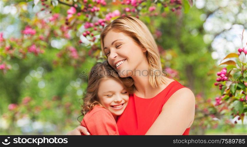 family, motherhood and people concept - happy smiling mother and daughter hugging over cherry blossom background. happy mother and daughter hugging over garden